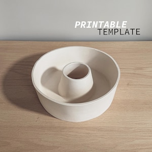 Puede incluir: Un molde de cerámica blanco, redondo, con un agujero en el centro. El molde está diseñado para hornear un pastel o una masa en forma de anillo. PRINTABLE TEMPLATE está escrito en texto negro en la parte superior de la imagen.