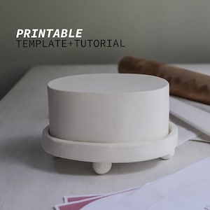 Peut inclure: Objet cylindrique en céramique blanche avec un dessus plat, posé sur une base assortie avec trois pieds arrondis. Le texte "PRINTABLE TEMPLATE+TUTORIAL" est affiché en blanc. Un rouleau à pâtisserie en bois est en arrière-plan.