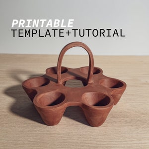 Könnte beinhalten: Ein terracottafarbener Eierhalter mit einem Griff. Der Halter hat sechs einzelne Fächer für Eier und einen Griff oben.