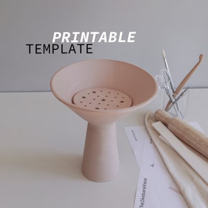 May include: A printable template for a pink ceramic ikebana vase with a round base and a wide, shallow bowl. The vase has a circular, perforated insert in the bowl.