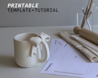 May include: White ceramic mug with a 3D bow handle. The mug is on a white surface with a printable template for a bow mug.