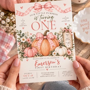 May include: A first birthday invitation card featuring a large orange pumpkin with a pink gingham bow, smaller pink and white pumpkins, floral accents, and text reading Our Little Pumpkin is Turning One, Emerson's First Birthday, and event details.