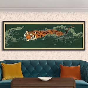 May include: A framed art print depicts a tiger swimming in green water with white-capped waves. The tiger has orange and black stripes, with a white face and chest. The artwork is in a black frame and is displayed above a blue sofa.