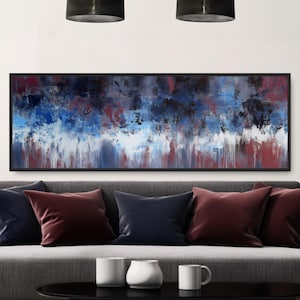 May include: Abstract art piece with a black frame. The artwork features a blend of blue, white, and red brushstrokes. The painting hangs above a gray sofa with burgundy and navy blue pillows. A black coffee table holds white mugs and a decorative vase.