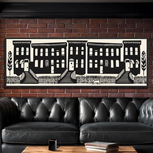 May include: Black and white art print of a row of townhouses. The artwork features a minimalist design with detailed windows, doors, and steps leading to each house. The print is framed in a black frame and is displayed on a brick wall.