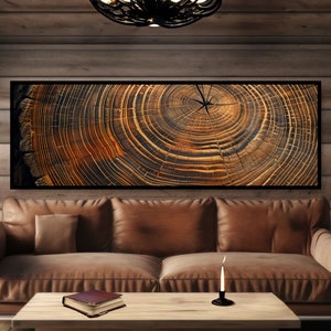 May include: A close-up of a wood grain pattern with concentric rings of brown and black. The wood grain is displayed in a framed picture hanging on a wall above a brown leather couch.
