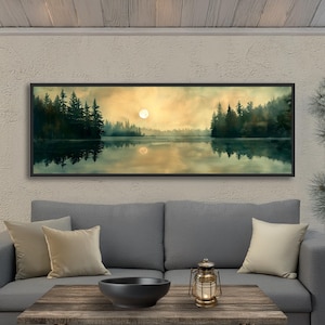 May include: A panoramic landscape wall art print featuring a calm lake reflecting a forest of dark green pine trees under a soft, golden-hued sky with a pale moon. The artwork is enclosed in a thin black frame, capturing a serene, misty atmosphere with muted tones and a horizontal composition.