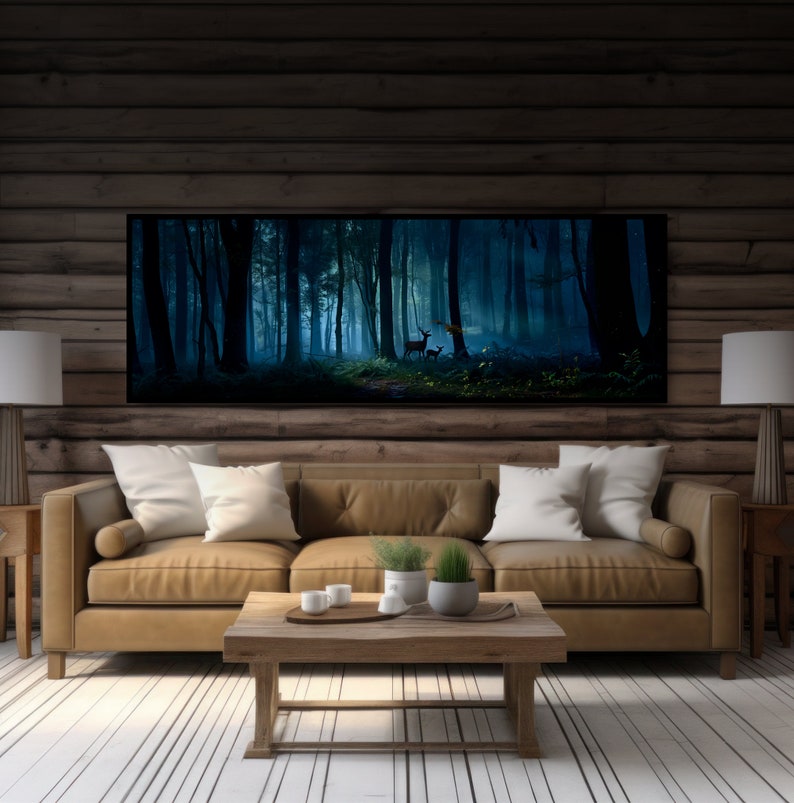 May include: A large framed art print depicting a misty forest scene with deer. The artwork hangs above a tan leather sofa with white pillows. The room has wooden walls and a light-colored wooden floor. Two lamps with white shades flank the sofa.