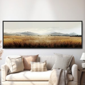 May include: A panoramic landscape photograph of a field of tall, golden grass with a distant mountain range in the background. The sky is a soft blue with white clouds.