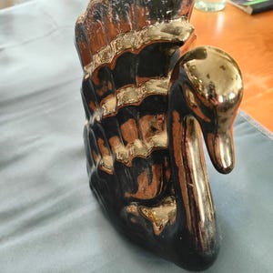 May include: A ceramic swan figurine with a black body and gold-colored accents on the wings and head. The swan has a curved neck and is positioned upright. The figurine is likely a decorative item for a home.