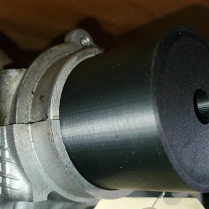 May include: A black cylindrical component inserted into a silver metallic part. The black cylinder has a central hole. The metallic part has a rough, textured surface. The image is well-lit, showing the contrast between the two materials.