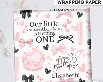 May include: Pink and black wrapping paper with a pattern of bows, hearts, and the text "Our little sweetheart is turning ONE" and "Happy Birthday Elizabeth!"