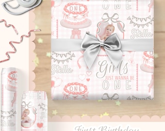 May include: A square gift wrapped in light pink and white plaid paper featuring illustrations of birthday cakes, banners, and the text "Girls Just Wanna Be One" and "Stella," finished with a large, shiny silver ribbon bow tied around the center.