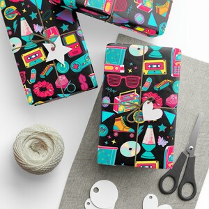 K&ouml;nnte beinhalten: Schwarzes und wei&szlig;es Geschenkpapier mit einem Retro-Thema der 90er Jahre. Das Papier zeigt eine Vielzahl von bunten Symbolen, darunter Kassetten, Rollschuhe, Boomboxen und Lavalampe.