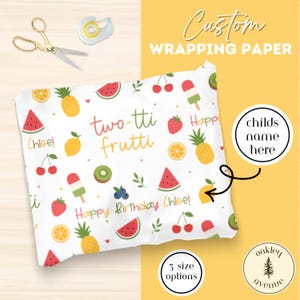 May include: White wrapping paper with a colorful fruit pattern, including watermelons, pineapples, and cherries. Text reads "two-tti frutti" and "Happy Birthday Chloe!" Gold scissors and tape dispenser are in the background.
