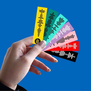 Può includere: Una mano tiene un ventaglio di carte colorate con motivi di onde sonore in bianco e nero. Le carte sono gialle, verdi, azzurre, viola, rosa, rosse e nere.