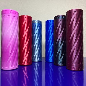 May include: A collection of cylindrical containers in various colors, including pink, red, light blue, dark blue, black, and purple. Each container has a textured, diagonal pattern and a matching lid. The containers are arranged on a reflective blue surface.