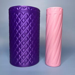 May include: Two cylindrical containers. One is a deep purple with a diamond pattern, and the other is a light pink with a spiral design. Both have a ridged top and bottom. The background is a light blue.