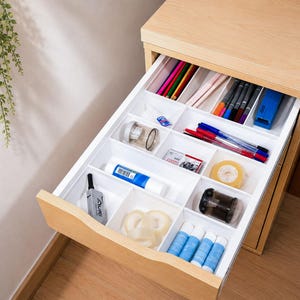 May include: A light wood desk drawer featuring a white plastic organizer tray with multiple compartments. The tray holds various office supplies including colored pencils, pens, glue sticks, adhesive tape rolls, a stapler, and a pencil sharpener.