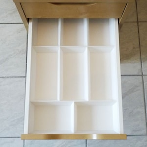 May include: A white drawer organizer with multiple compartments. The organizer is made of plastic and has a smooth, white finish. The drawer organizer is designed to help keep drawers organized and tidy.