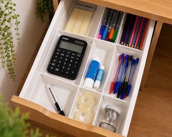 May include: A light wood desk drawer featuring a white plastic organizer tray with multiple compartments. The tray contains a black Casio calculator, colored pencils, ballpoint pens, glue sticks, adhesive labels, tape rolls, a utility knife, and a sharpener.
