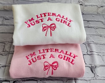 May include: Two sweatshirts with the text "I'm literally just a girl" in pink lettering with a pink bow. The top sweatshirt is white and the bottom sweatshirt is pink.