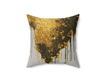 Puede incluir: Una almohada cuadrada con fondo gris y un diseño abstracto en negro y dorado. El diseño presenta una gran forma dorada brillante que gotea con acentos negros.