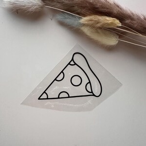 Könnte beinhalten: Ein transparenter Aufkleber mit einer schwarzen Strichzeichnung eines einzelnen Stücks Pepperoni-Pizza. Das Design besteht aus einem dreieckigen Krustenrand und mehreren kreisförmigen Pepperoni-Formen, die schwarz auf einem transparenten Träger umrandet sind.