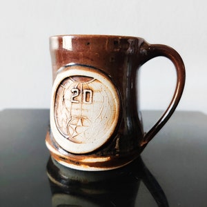 May include: A brown ceramic mug with a white design featuring a globe and the number "20".