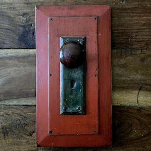May include: A red wooden door frame with a dark brown door knob and a keyhole. The door frame is distressed and has a rustic look.
