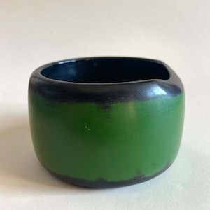 May include: A wide, circular bangle bracelet featuring a smooth, matte finish. The exterior displays a vibrant green band across the centre, bordered by dark black edges at the top and bottom. The interior of the bracelet is solid black.