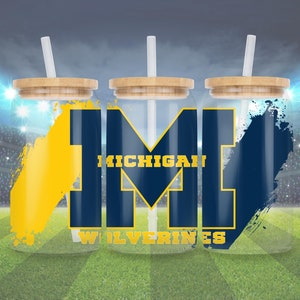 Op de afbeelding: Drie transparante bekers met een houten deksel en een rietje. Elke beker heeft een blauwe en gele afbeelding met de tekst "MICHIGAN WOLVERINES".