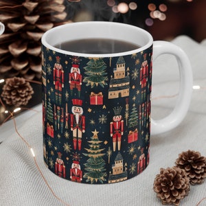 May include: A white ceramic mug with a blue background and a repeating pattern of nutcracker soldiers, Christmas trees, and stars. The mug is filled with a dark liquid and steam is rising from the top.