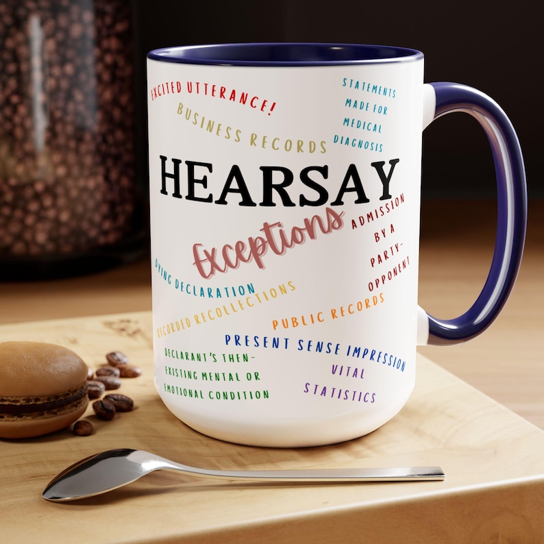 May include: White ceramic mug with a blue rim and handle. The mug features the word "HEARSAY" in black text and the word "Exceptions" in pink text. The mug also features a variety of legal terms related to hearsay exceptions, including "Excited Utterance", "Business Records", "Statements Made for Medical Diagnosis", "Dying Declaration", "Recorded Recollections", "Admission by a Party-Opponent", "Public Records", "Present Sense Impression", "Declarant's Then-Existing Mental or Emotional Condition", and "Vital Statistics".