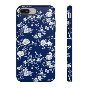 Peut inclure: Une coque de t&eacute;l&eacute;phone bleue avec un motif floral blanc. La coque a un rebord sur&eacute;lev&eacute; autour de l'objectif de l'appareil photo et une d&eacute;coupe pour le port de charge.