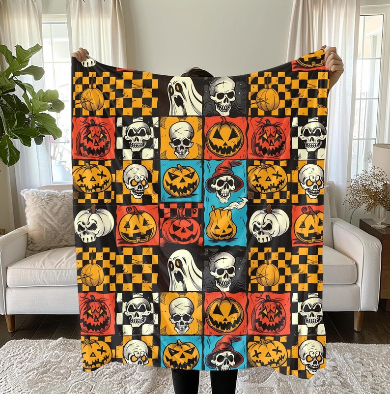 May include: A Halloween-themed fleece blanket with a repeating pattern of orange and yellow pumpkins, black and white chequered squares, and white ghosts with skulls. The blanket features a variety of skull designs, including those with crossbones, top hats, and wings.