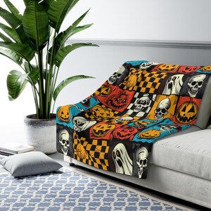 May include: A black and orange Halloween themed throw blanket with a patchwork design featuring skulls, pumpkins, ghosts, and chequered patterns.