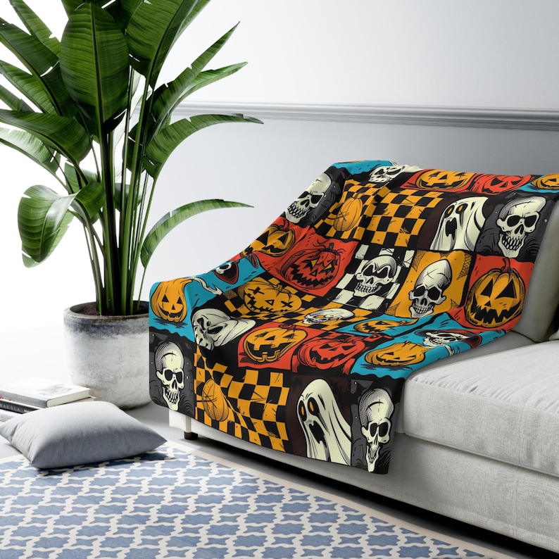 May include: A black and orange Halloween themed throw blanket with a patchwork design featuring skulls, pumpkins, ghosts, and chequered patterns.