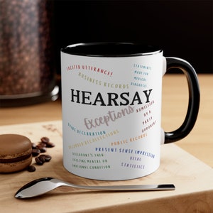 May include: White ceramic coffee mug with a black rim and handle. The mug features a black and white word cloud design with the word "HEARSAY" in large, bold letters. The word cloud includes legal terms related to hearsay exceptions.