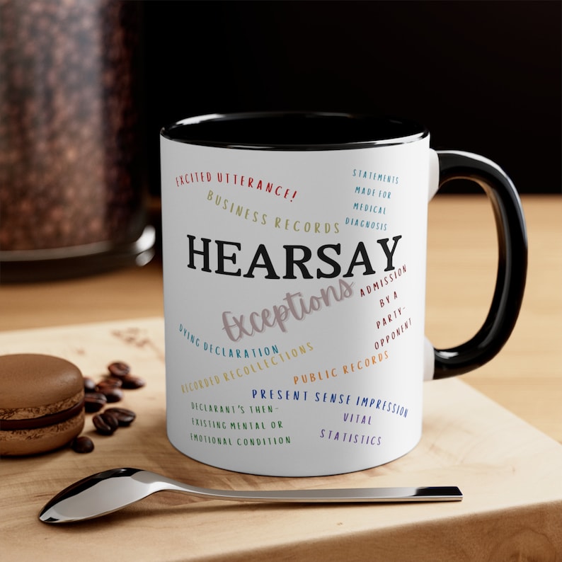 May include: White ceramic coffee mug with a black rim and handle. The mug features a black and white word cloud design with the word "HEARSAY" in large, bold letters. The word cloud includes legal terms related to hearsay exceptions.