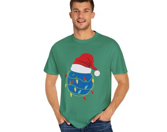 May include: A green t-shirt featuring a blue bowling ball wearing a red and white Santa hat and surrounded by colourful Christmas lights.