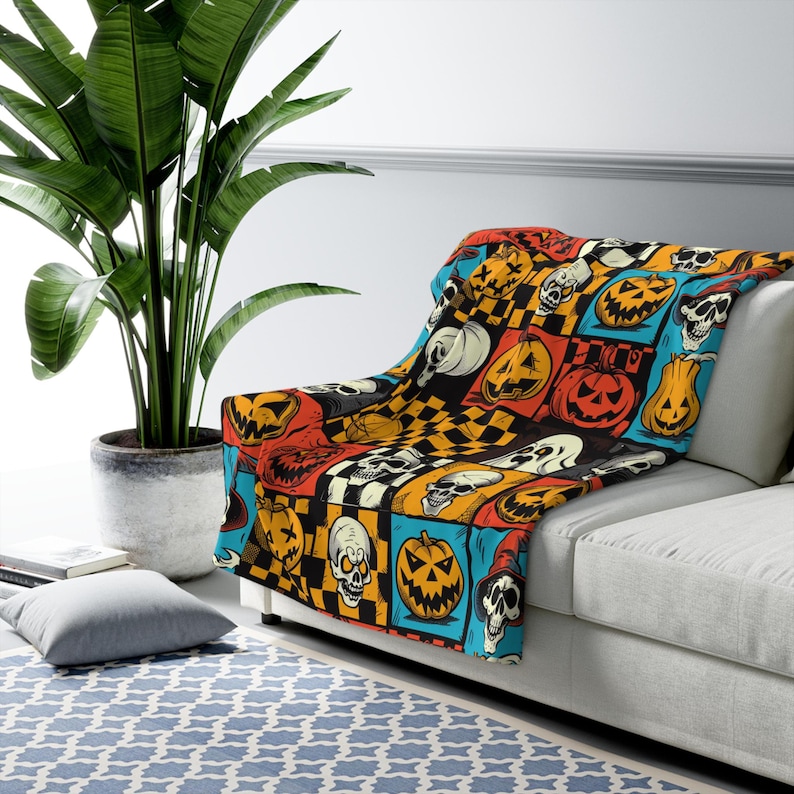 May include: A colourful throw blanket with a Halloween theme. The blanket features a repeating pattern of orange pumpkins, black skulls, and chequered squares.