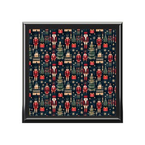May include: A square, black-framed decorative tray with a repeating pattern of red and white nutcrackers, green Christmas trees, and gold stars on a dark blue background. Red gift boxes and buildings are also featured in the design.