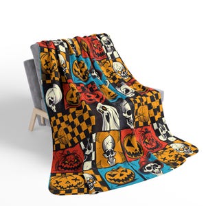 May include: A colourful Halloween-themed throw blanket with a patchwork design featuring skulls, pumpkins, and checkerboard patterns.