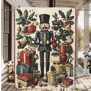 May include: A festive Christmas-themed blanket featuring a black nutcracker soldier surrounded by holly, ornaments, and wrapped gifts in red, green, and gold. The blanket is rectangular and has a red border.