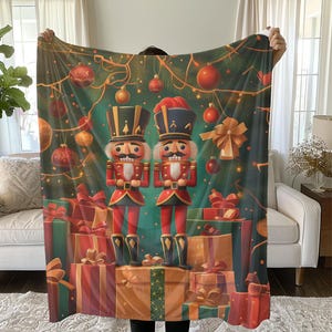 May include: A festive Christmas throw blanket featuring two nutcracker soldiers standing in front of a Christmas tree decorated with ornaments and presents. The nutcrackers are wearing traditional red and gold uniforms and holding their weapons.