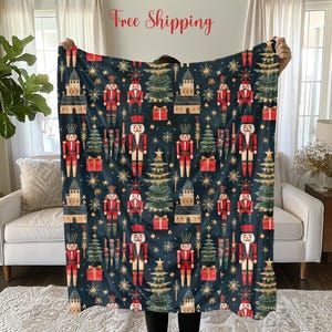 May include: A navy blue fleece throw blanket with a repeating pattern of nutcracker soldiers, Christmas trees, and stars. The pattern is in shades of red, green, gold, and white.