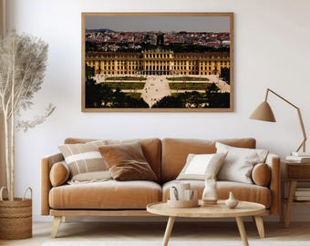 May include: A framed photograph of a large, yellow building with a symmetrical design. The building is surrounded by a courtyard with trees and walkways. The photograph is hanging on a white wall above a brown couch with pillows.