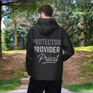 May include: Black hooded jacket with the words "PROTECTOR PROVIDER Priest" printed in white and gray. The jacket is worn by a person standing in front of a blurred background of trees and a walking path.