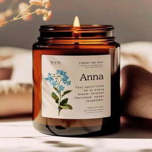 May include: A brown glass candle jar with a white label. The label features a forget-me-not flower illustration and the text "FORGET-ME-NOT A symbol of remembrance, love, and memories. Anna Your spirit lives on in every bloom, forever cherished, never forgotten. MADE WITH LOVE 9oz. Cashmere Musk NATURAL COCONUT WAX"